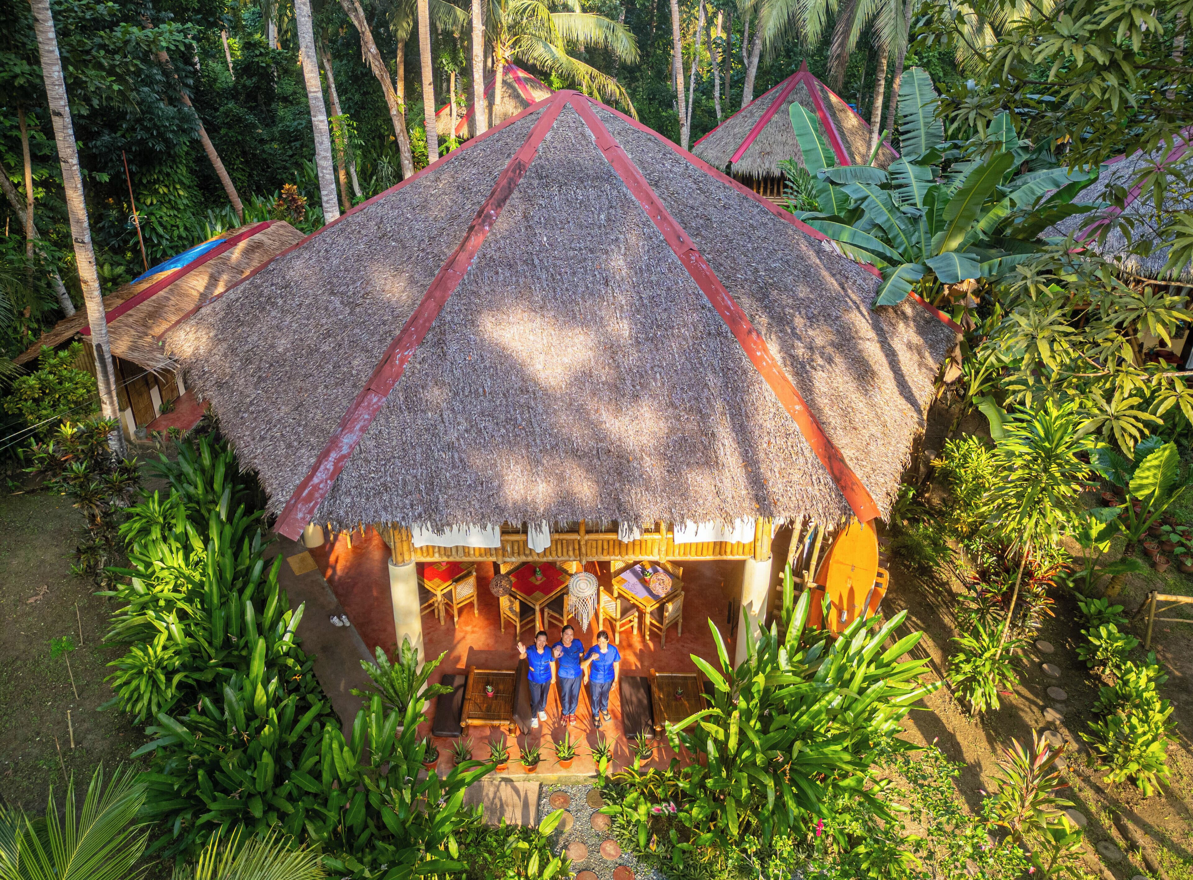 A thatched-roof hut with a red trim, surrounded by lush tropical vegetation.