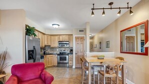 A compact kitchen with wooden cabinets, stainless steel appliances, and a dining area with a wooden table and chairs. - Peaceful Oceanfront OBX Getaway (Kill Devil Hills)