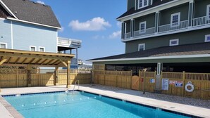 A swimming pool with a wooden deck and a covered area, surrounded by a wooden fence and a building with balconies. - Peaceful Oceanfront OBX Getaway (Kill Devil Hills)