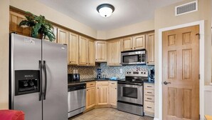 A kitchen with wooden cabinets, stainless steel appliances, a microwave, and a refrigerator. - Peaceful Oceanfront OBX Getaway (Kill Devil Hills)