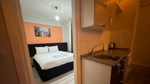 A compact hotel room with a bed, a small kitchenette, and a painting on the wall. - Vast Apart Otel (Izmir)