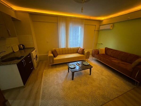 Un espacio habitable compacto con sofá, mesa de centro y zona de cocina que incluye una lavadora.
