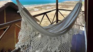 Una hamaca suspendida bajo una estructura de madera, con vista a la playa y al océano.