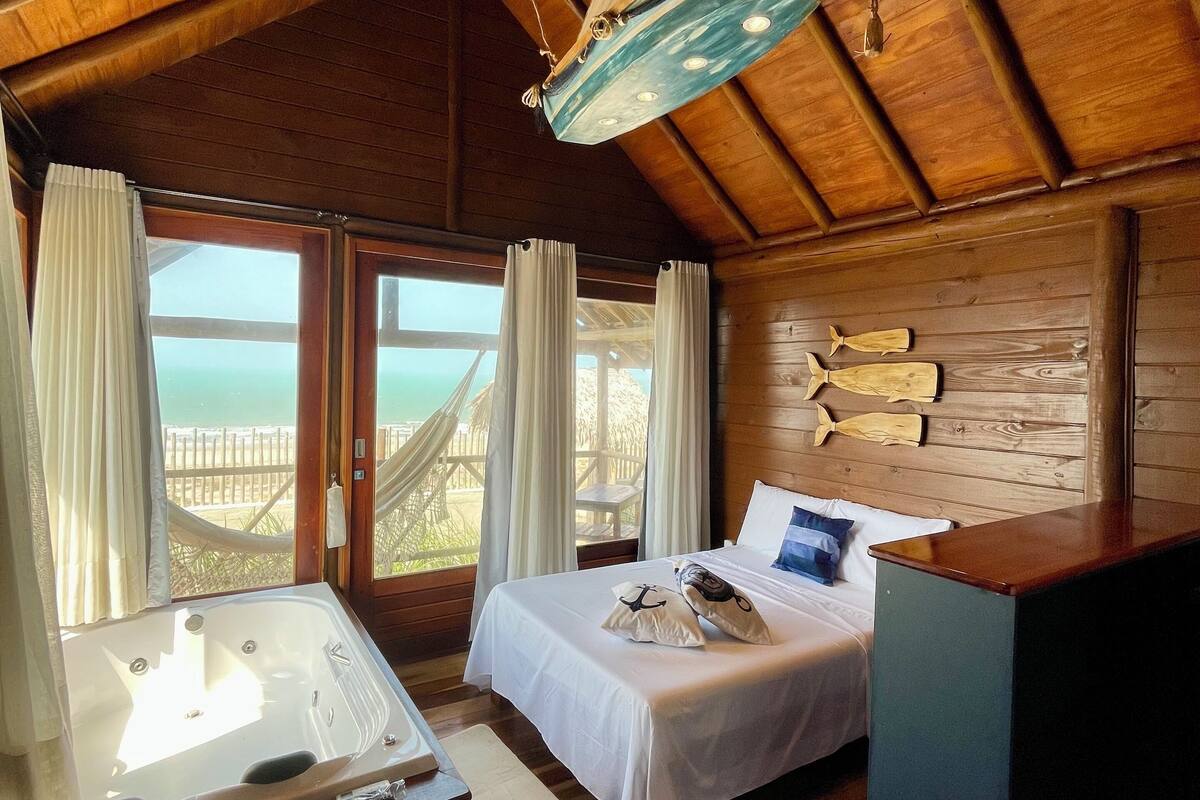 Una cabaña de madera con una cama, un escritorio pequeño y vistas a la playa.