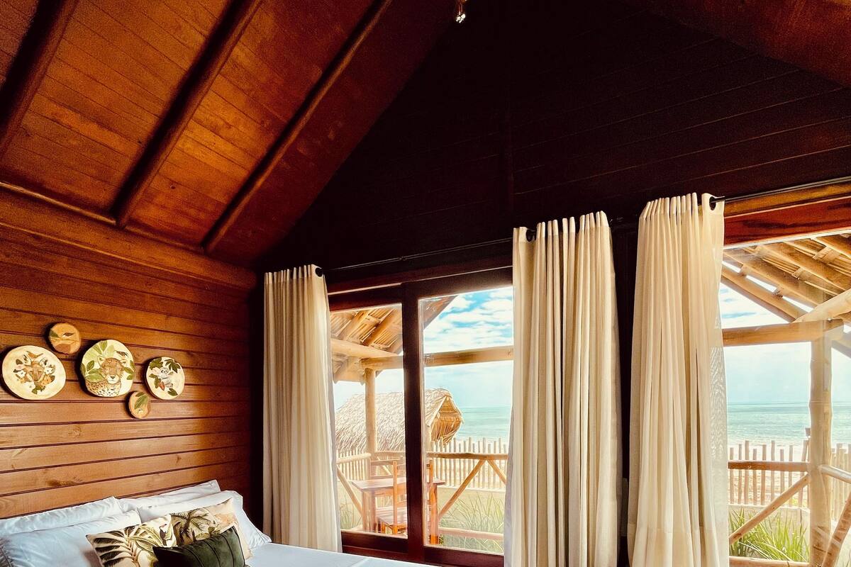 Una habitación de cabaña de madera con cama, bañera y vista al océano.