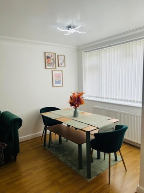 A dining area with a table, chairs, a vase with flowers, and framed pictures on the wall. - Spacious 4-Bed House I Free Parking & Fast Wi-Fi (Dagenham)