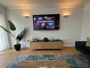 A modern living room with a flat-screen TV, wooden console, potted plants, and a green sofa. - Spacious 4-Bed House I Free Parking & Fast Wi-Fi (Dagenham)