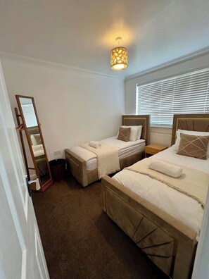 A bedroom with two beds, a mirror, a bedside table, and a hanging light fixture. - Spacious 4-Bed House I Free Parking & Fast Wi-Fi (Dagenham)