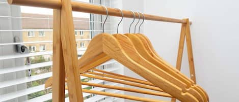 A wooden drying rack with multiple pegs, positioned in front of a window with blinds.