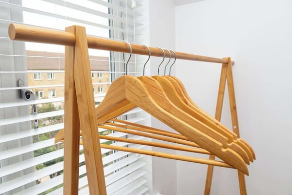 A wooden drying rack with multiple pegs, positioned in front of a window with blinds.
