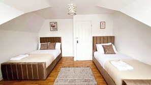 A room with two beds, a wooden floor, a white door, and a ceiling light fixture. - Spacious 4-Bed House I Free Parking & Fast Wi-Fi (Dagenham)