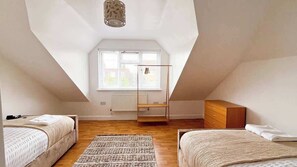 Ein Schlafzimmer mit schrägem Dach, einem Fenster, einer Heizung, einer Holzkommode und zwei Betten.