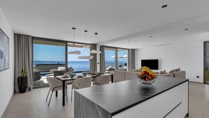 Una sala de estar moderna con una isla grande, comedor y vista al mar.