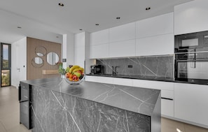 A modern kitchen with a marble island, built-in appliances, and a large window. - Luxurious home in Makarska with sauna (Makarska)