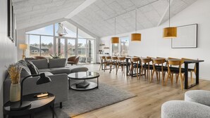 Un salon spacieux avec une grande fenêtre, un coin repas avec des chaises en bois et un ensemble de canapés modernes.