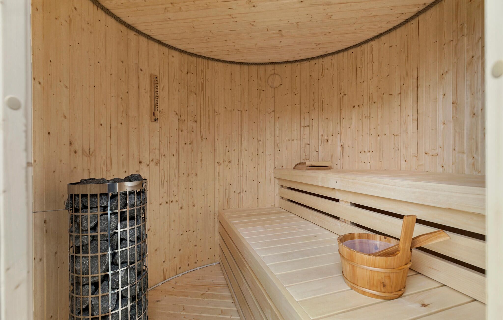 A sauna with wooden walls and benches, a metal container with rocks, and a wooden bucket.