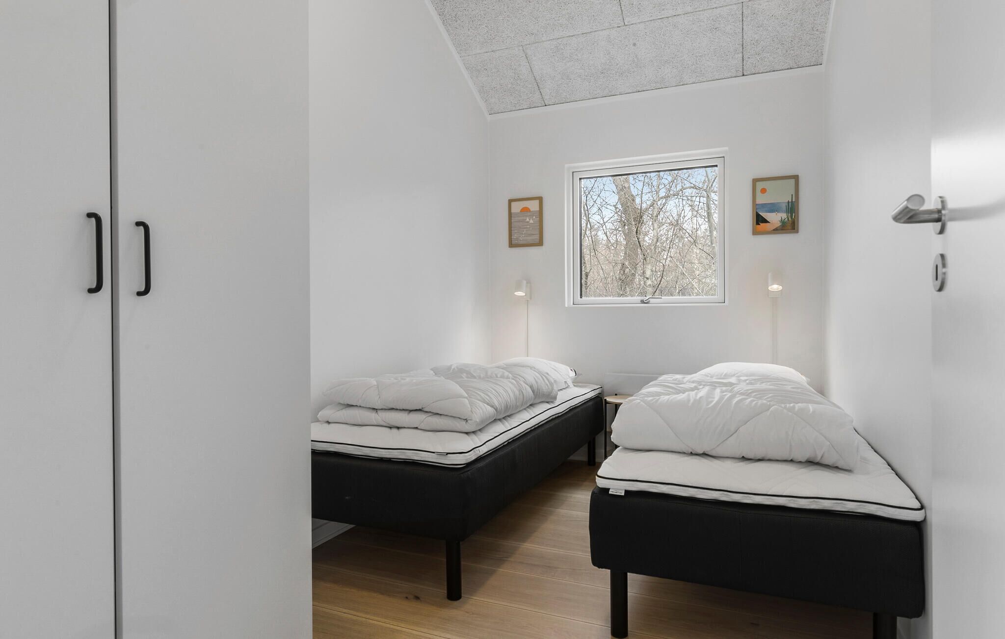 A modern bedroom with two single beds, a skylight, and a large window with a view of trees.