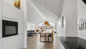 Une cuisine moderne dotée d’un grand îlot central, d’un four encastré et d’un coin repas avec une longue table et des chaises.