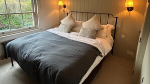 Ein Schlafzimmer mit einem großen Bett, zwei Wandlampen und einem Fenster mit Blick auf Grünflächen.