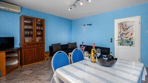 Een kamer met een eettafel gedekt voor twee personen, een kast met glazen deuren, een bank en een televisie.