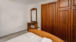 Een slaapkamer met een bed, een houten garderobe, een spiegel en een klein nachtkastje.