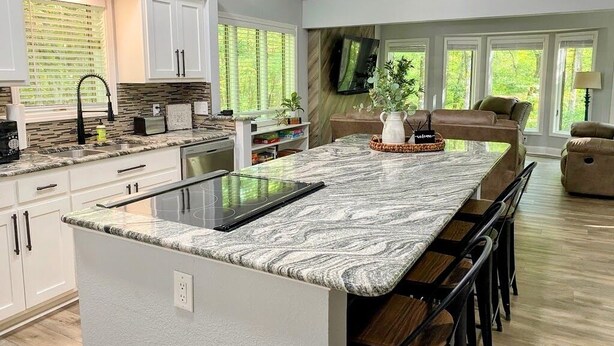 Una cocina moderna con una isla grande, armarios blancos y un comedor con sofá y sillas.