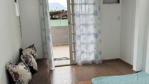 Een kamer met een bed, een bank met kussens, een raam met gordijnen en een deur naar buiten.