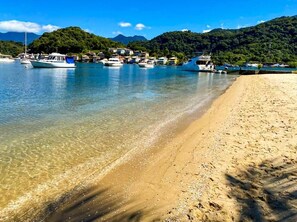 Ein Strand mit klarem Wasser, Booten und einer gebirgigen Kulisse.