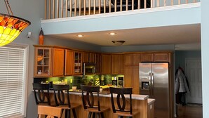 A modern kitchen with a central island, wooden bar stools, and a stainless steel refrigerator.