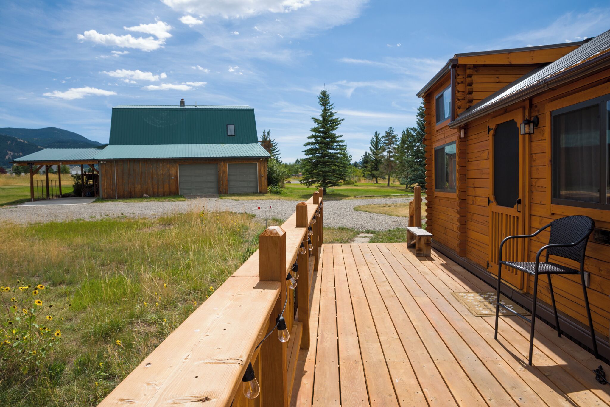 A wooden deck leading to a cabin with a green roof, a covered area with a bench, and a chair on the deck.