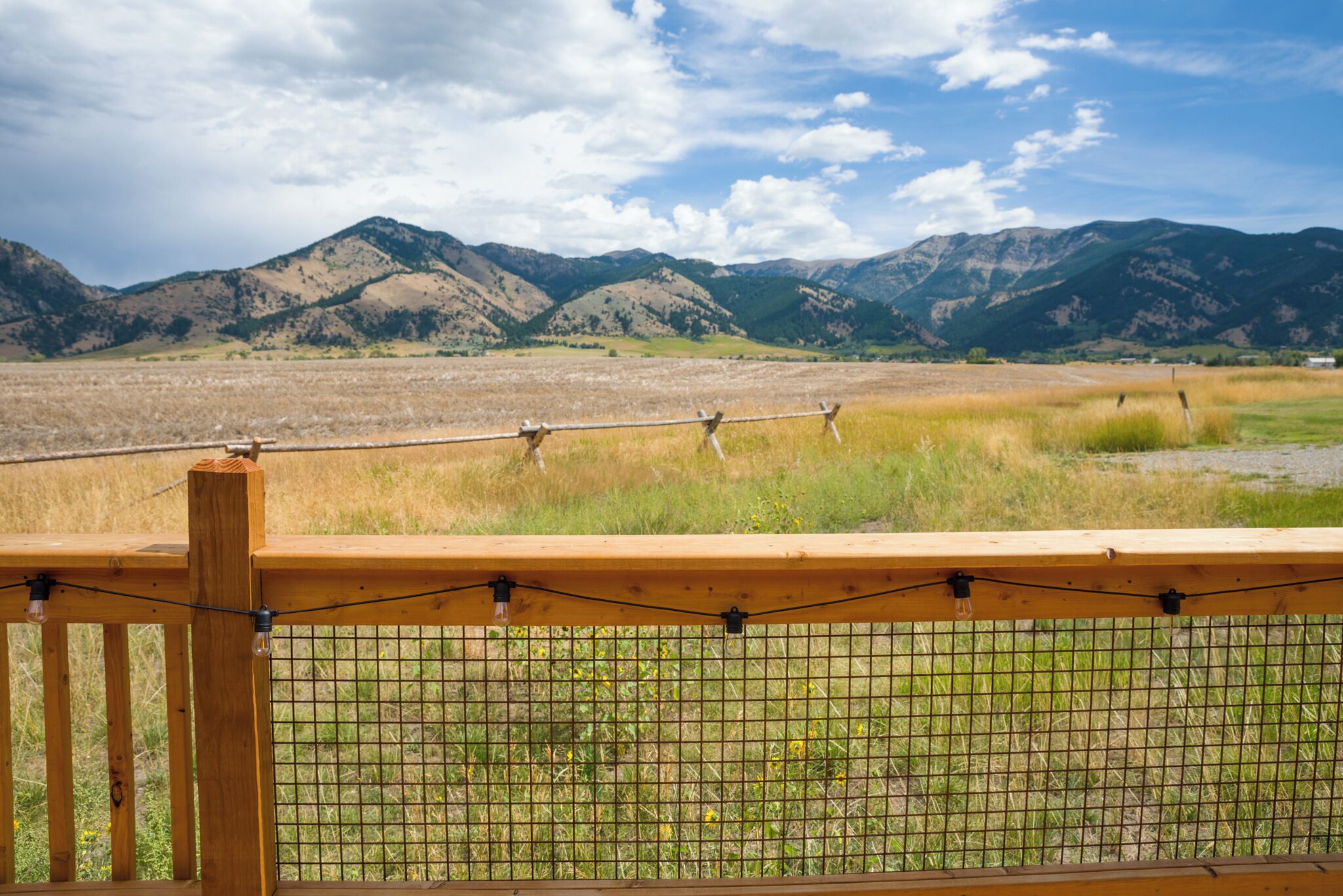 Una cerca de madera con una celosía metálica, con vistas a un paisaje montañoso y campos cubiertos de hierba.
