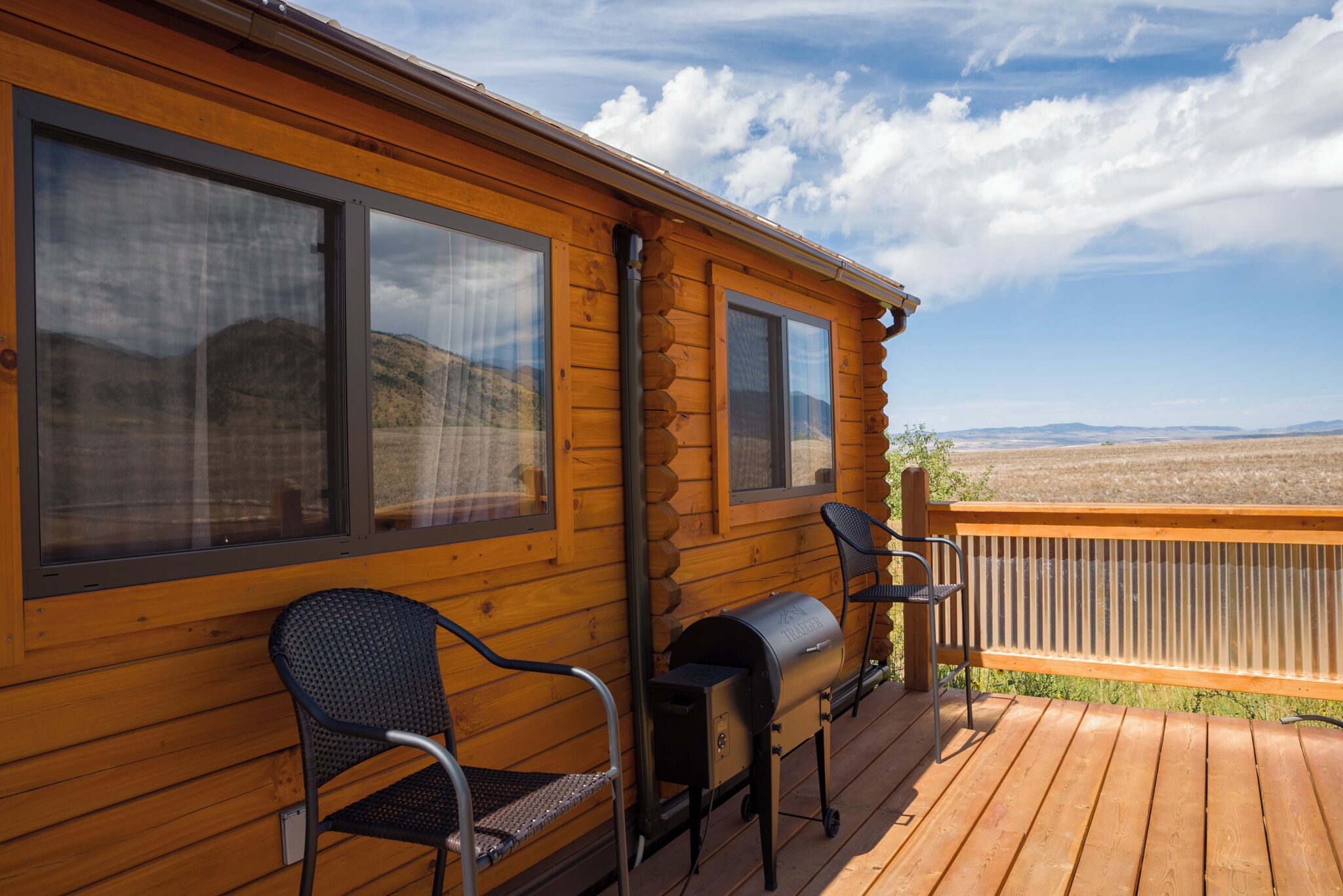 A wooden cabin with large windows, a deck, and a grill.