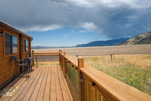 Eine Holzterrasse mit Sitzgelegenheit, mit Blick auf eine weite Landschaft und Berge in der Ferne.