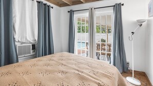 A bedroom with a bed, a window with curtains, a ceiling fan, and a view of the outdoors.
