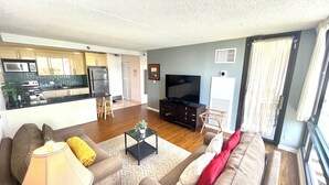 A living room with a sofa, a TV, and a kitchen in the background.