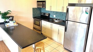 A compact kitchen with a black countertop, stainless steel appliances, and teal backsplash tiles.