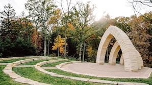 Un arco de piedra en un parque con un camino de ladrillo circular que conduce a él.