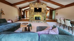 Un salón amplio con chimenea de piedra, ventilador de techo y televisión montada en la pared.