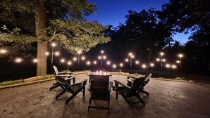 Un patio al aire libre con un brasero, rodeado de sillas y luces colgantes.