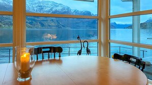 Ein Tisch mit Stühlen und einer Kerze in einem Zimmer mit großen Fenstern mit Blick auf einen See und Berge.