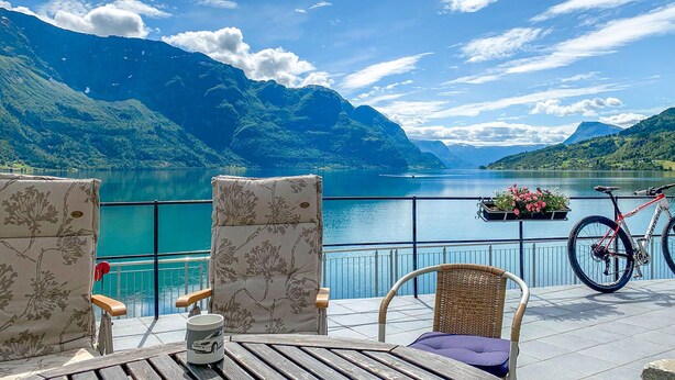Eine Terrasse mit Blick auf einen See und Berge, ausgestattet mit Liegestühlen, einem Fahrrad und einem Blumentopf.