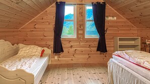 Ein gemütliches Schlafzimmer im Dachgeschoss mit zwei Betten, Holzwänden und einem Fenster mit Vorhängen.