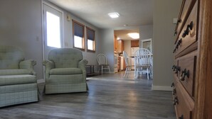 A spacious living room with a large green armchair, a smaller armchair, and a wooden dresser with multiple drawers.