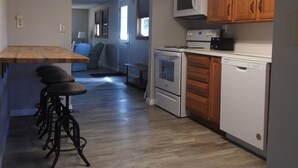 A kitchen with wooden cabinets, a microwave, a stove, and a dishwasher. There is a wooden dining table with bar stools.