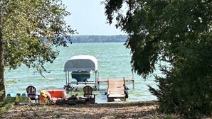 A lakeside setting with a covered boat dock, wooden chairs, and a picnic table.