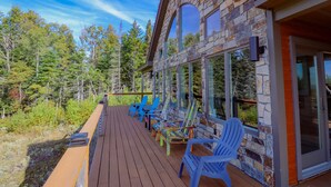 A wooden deck with blue chairs and skis, surrounded by stone walls and glass doors, overlooking a forest. - Lodges #72 - Rangeley Lake Overlook - ATV, Snowmobile, and close to Saddleback! (Rangeley)