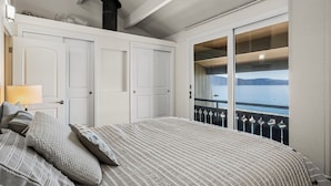 Un dormitorio con cama, mesita de noche, lámpara y vistas al mar a través de una puerta corredera.