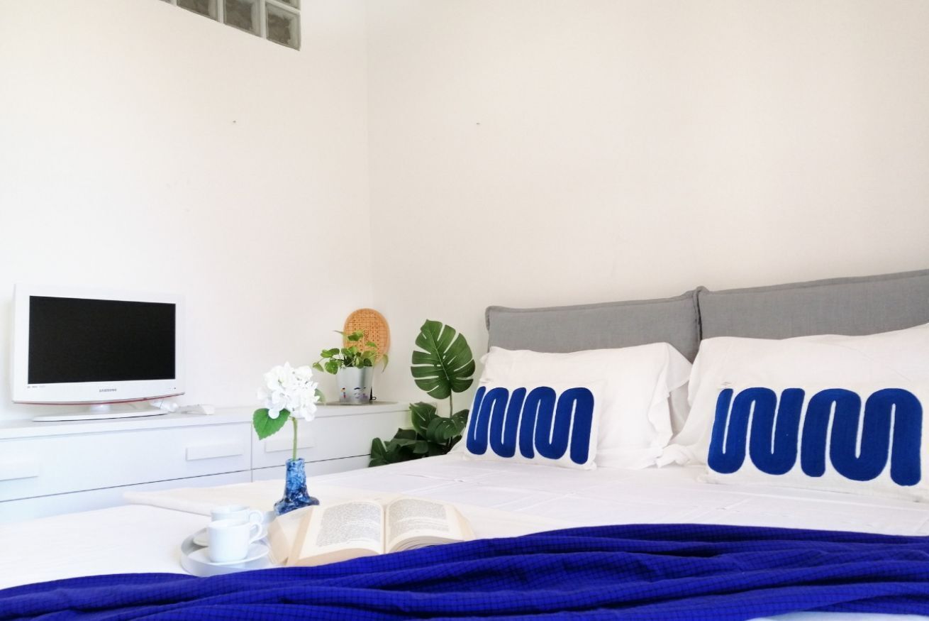 A neatly arranged bedroom with a bed, a bedside table with a book, a cup, and a plant.