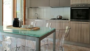 A modern kitchen with a glass table, clear chairs, a stove, and a built-in oven. - Holihome_The Lemon Garden (Tortoreto Lido)