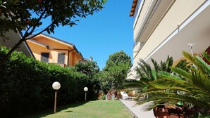 A narrow garden pathway flanked by lush greenery and a building with a yellow facade. - Holihome_The Lemon Garden (Tortoreto Lido)